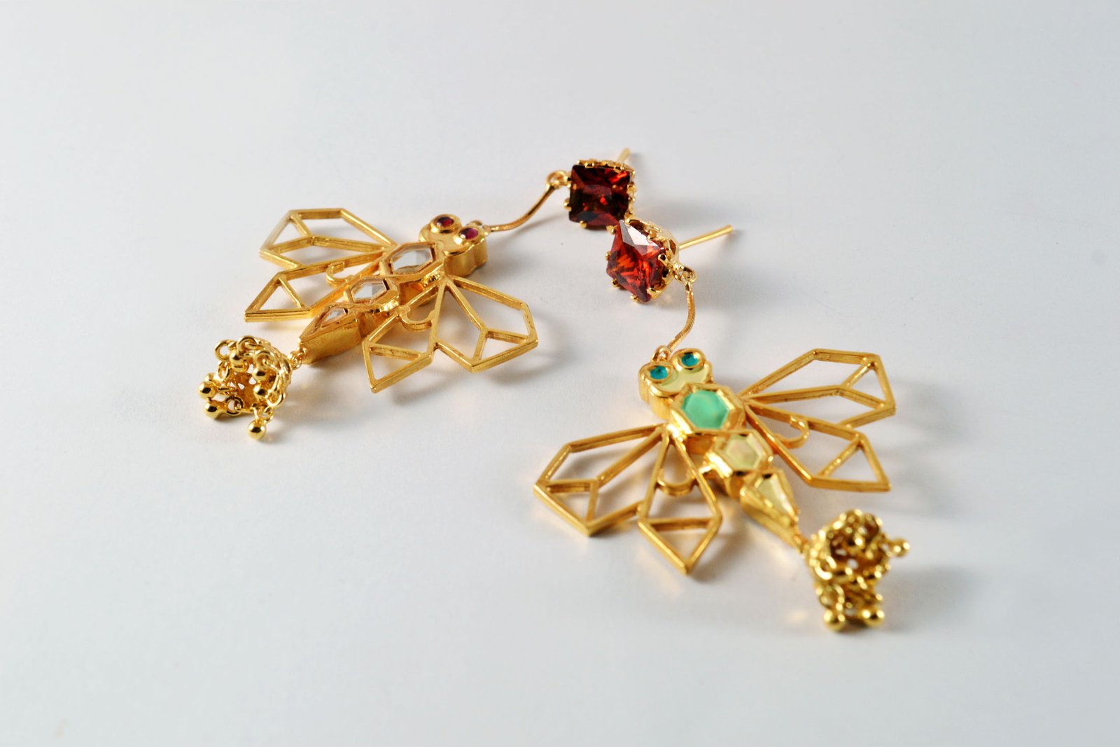 A pair of Safari dragonfly earrings in gold-plated silver with red zircon tops and pearl jhumki drops, on a pale grey ground.
