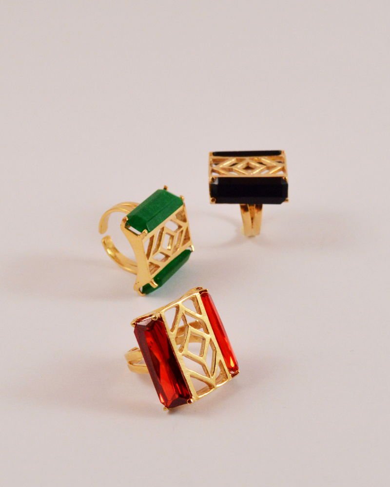 Two Statement Rings shown together: one set with a green jade bar and one with a red zircon bar, each in an open architectural cage.