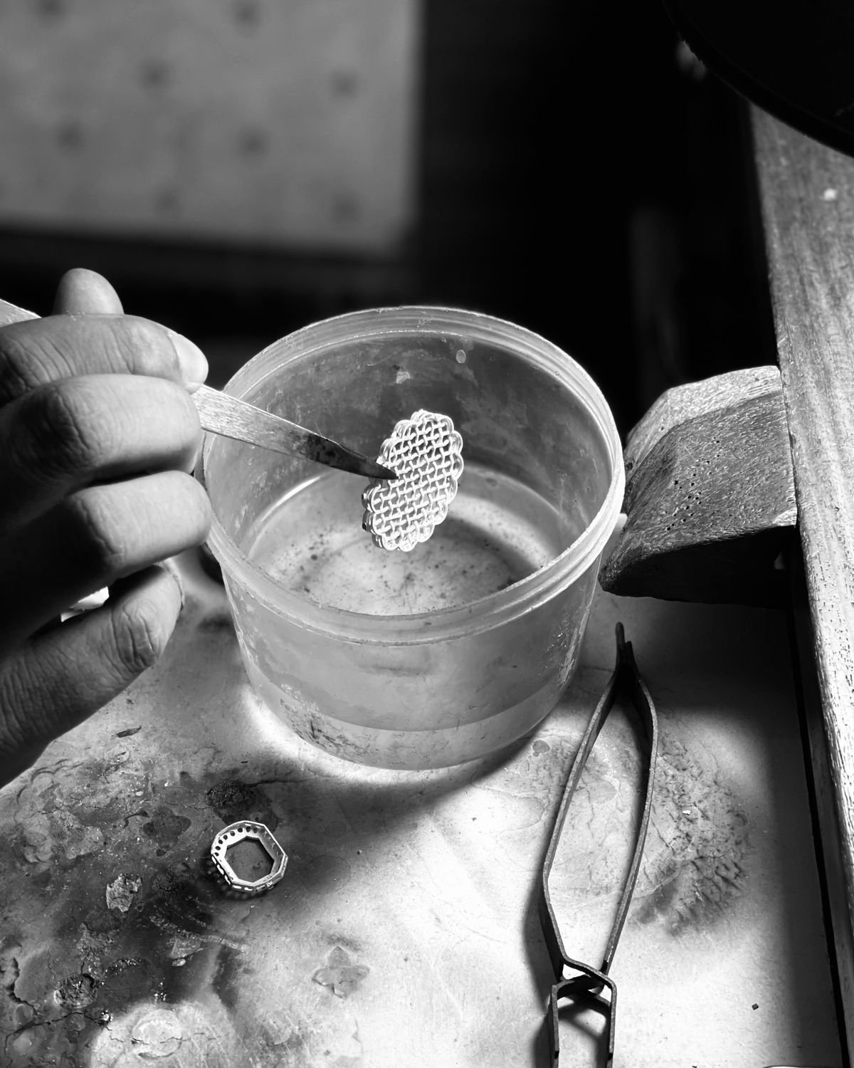 A hand lifting a filigree component out of a tub of cleaning solution with tweezers, above the soldering block.
