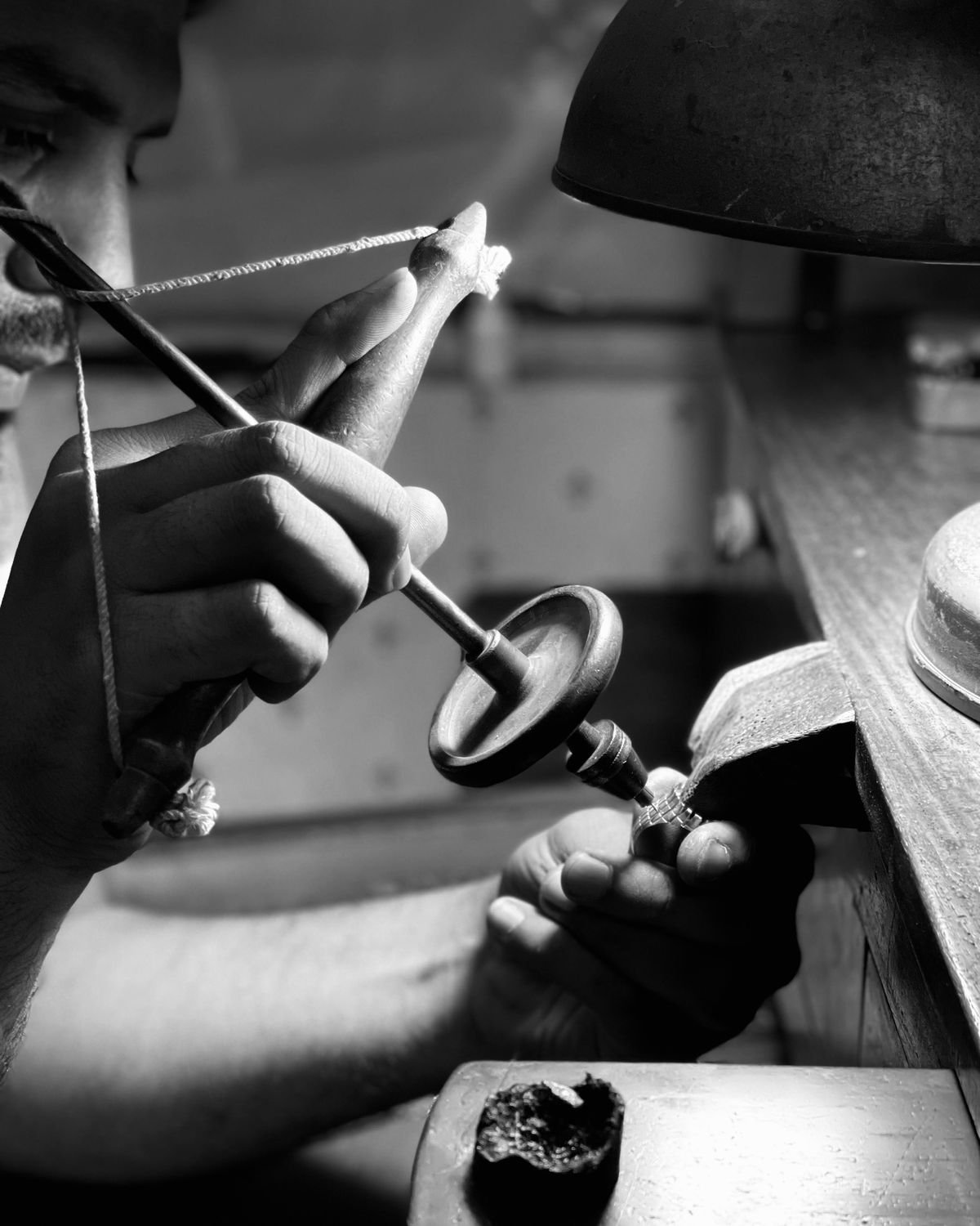 Two hands working a hand drill to pierce a small silver component held against the bench pin.