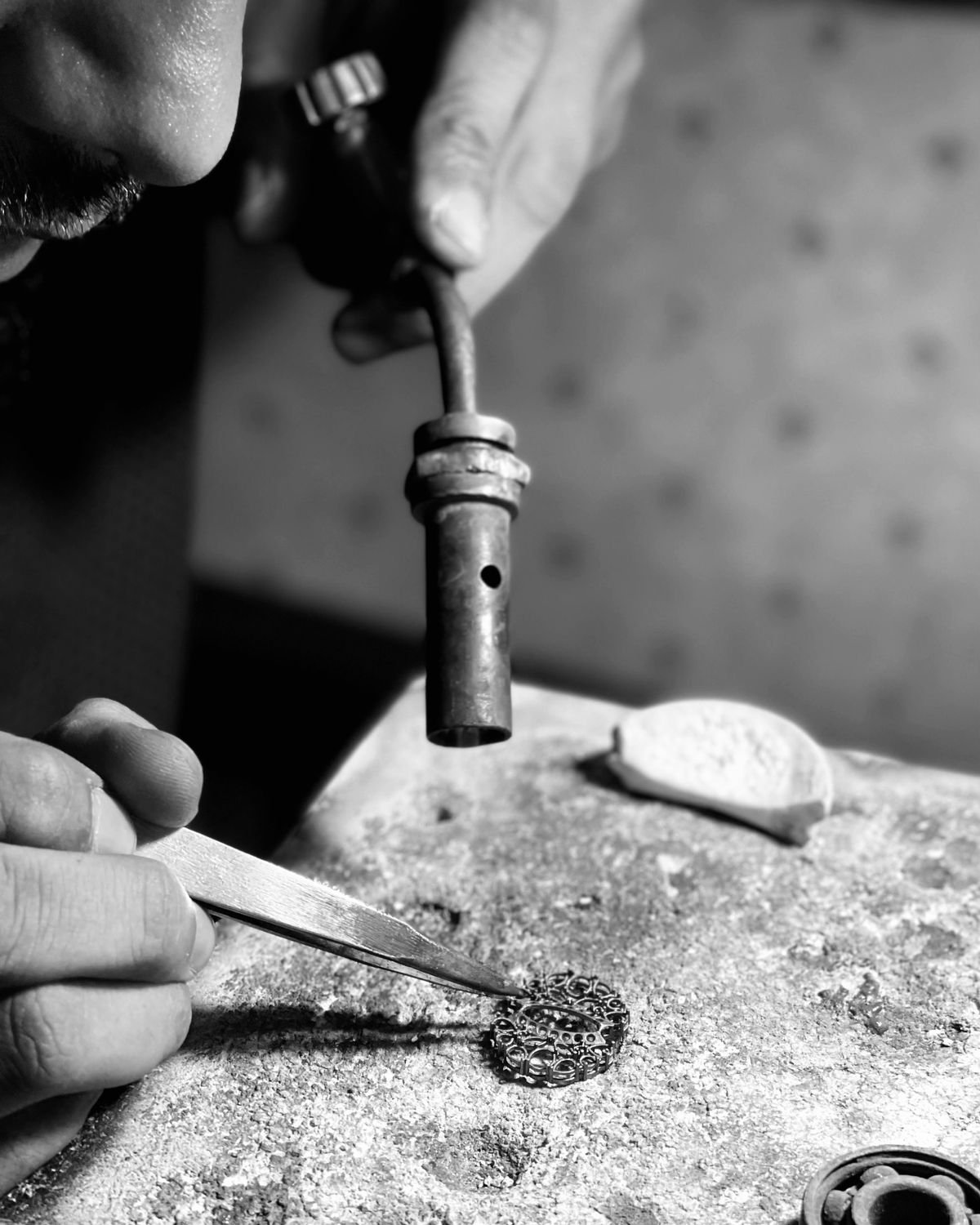 An artisan directing a blowpipe flame at a filigree piece held with tweezers on the soldering block.